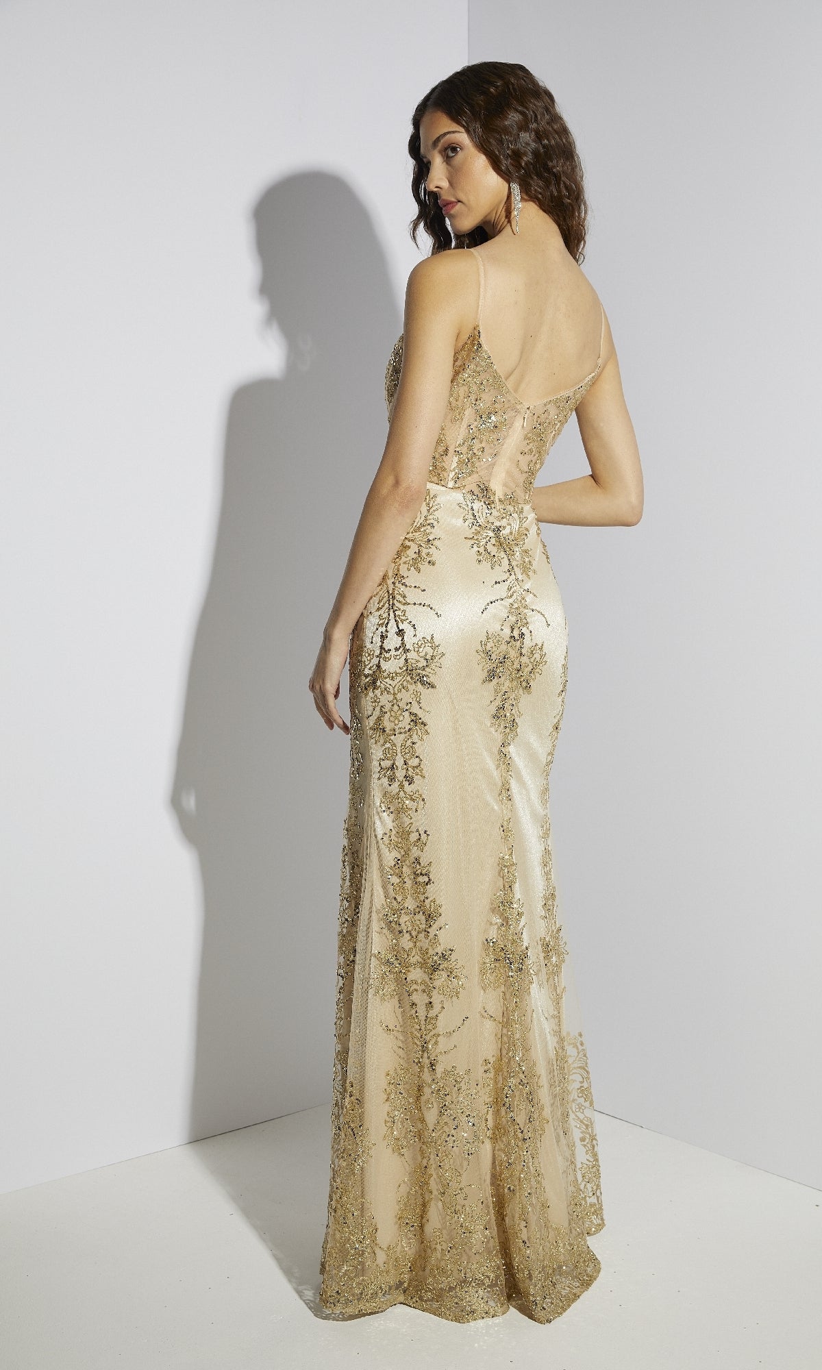 A woman stands facing away in a floor-length gold Long Glitter Jersey Prom Dress, Eureka 9188, featuring sheer panels and intricate embroidery, set against a minimalist white background.